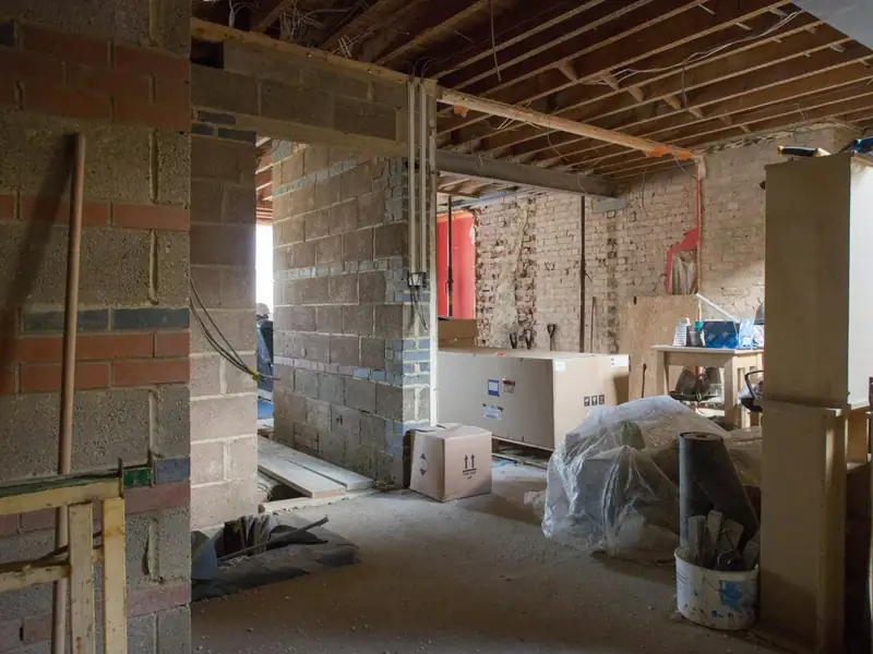 Maison vidée avant rénovation : plafond ouvert, murs en blocs, matériaux protégés