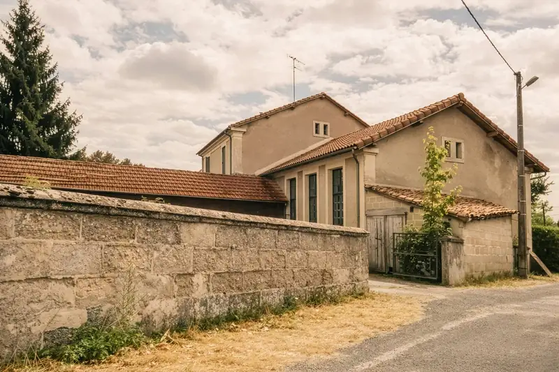 Maison rurale enduite sous un toit de tuiles, mur de clôture en pierre au bord de la route