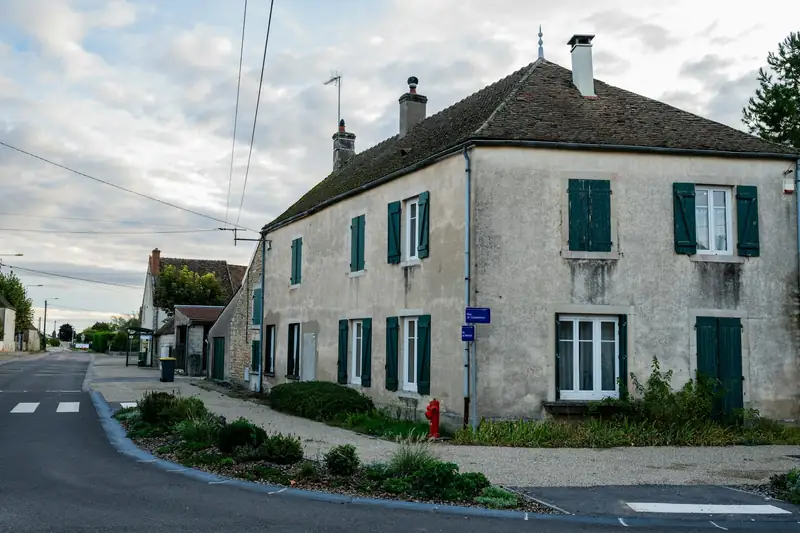 Maison ancienne enduite, volets verts, au carrefour d’une petite route