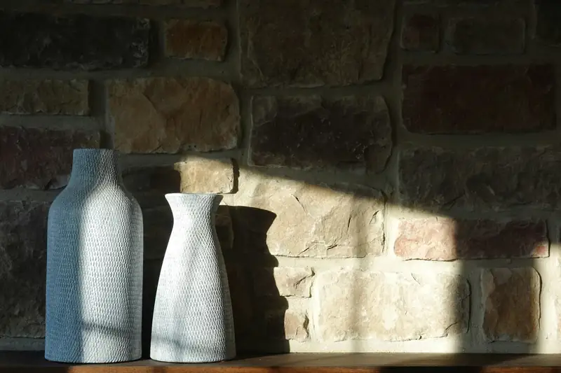 Mur en pierre apparente frappé par le soleil, deux vases en céramique blanche