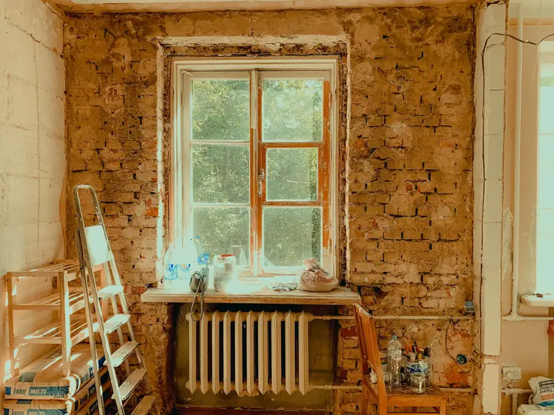 Pièce en cours de rénovation : murs mis à nu jusqu’à la brique, fenêtre ancienne et radiateur