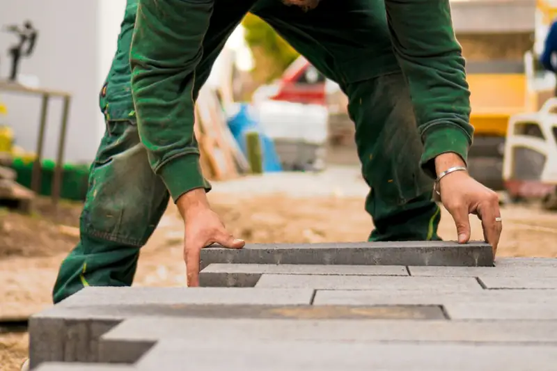 Poseur penché qui ajuste des pavés en béton sur leur lit de pose
