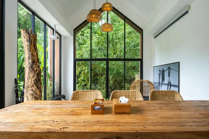 Grande table en bois sous une baie vitrée en pignon, sol clair d’un seul tenant